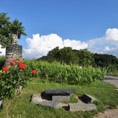 Kunstwerk auf dem Erlebnispfad Steinflasche umgeben von Rosen und Weinbergen