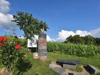 Kunstwerk auf dem Erlebnispfad Steinflasche umgeben von Rosen und Weinbergen