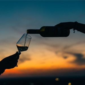 Vor dem Abendrot wird ein Glas Wein eingeschenkt. Dunkle Umrisse